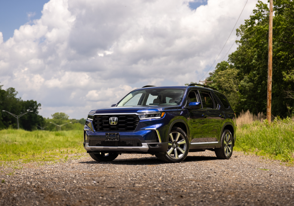 Blue 2025 Honda Pilot parked on a gravel road with trees in the background